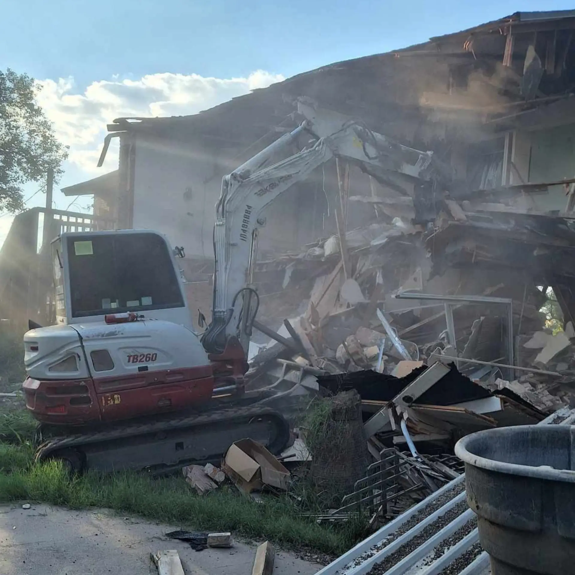 Excavator bringing down a two-story brick building in a cloud of dust