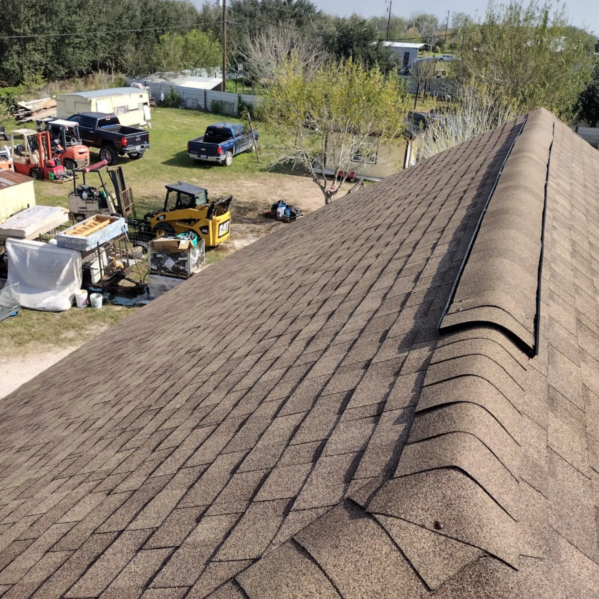Newly shingled roof above a job site with trucks and equipment