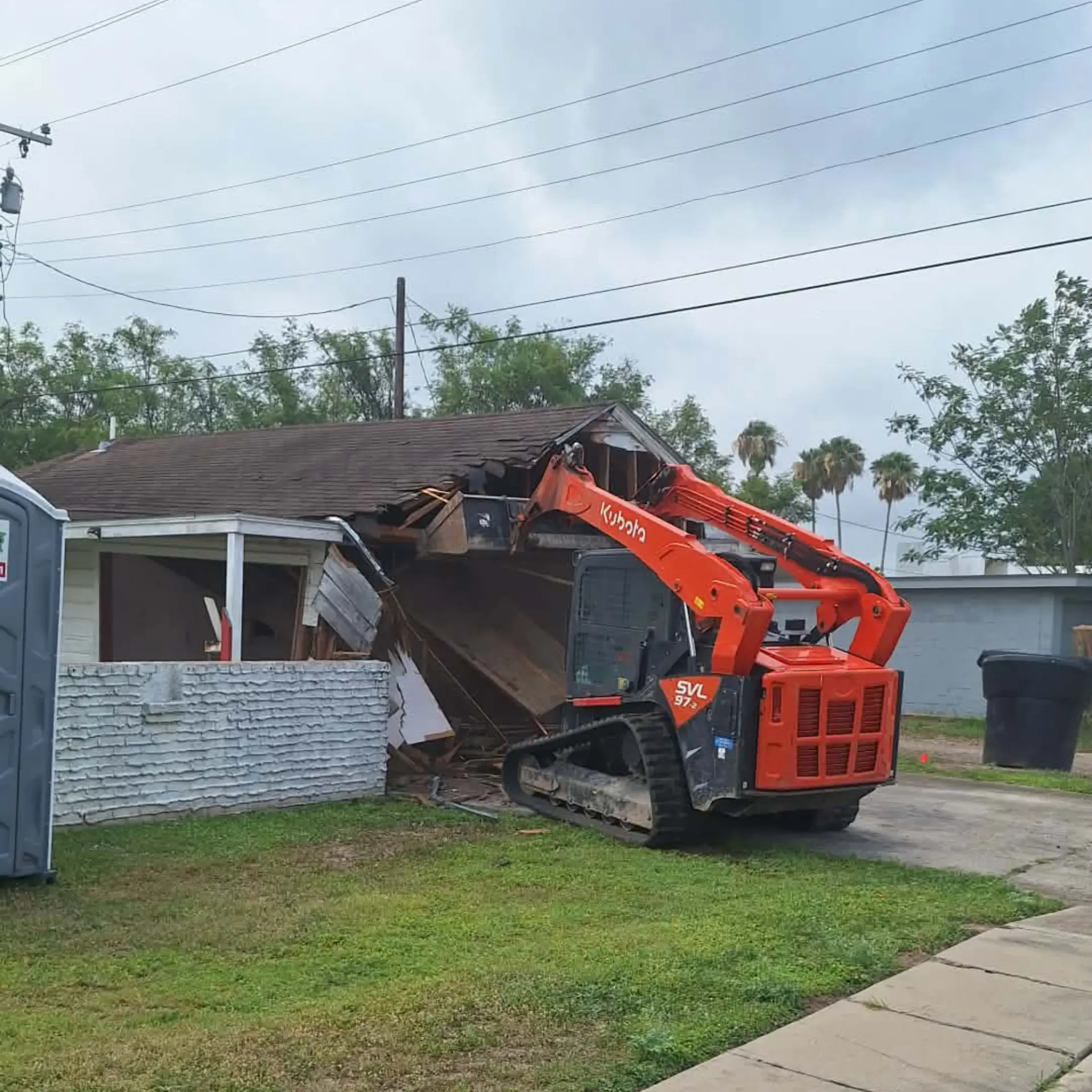 Track loader demolishing a white brick carport