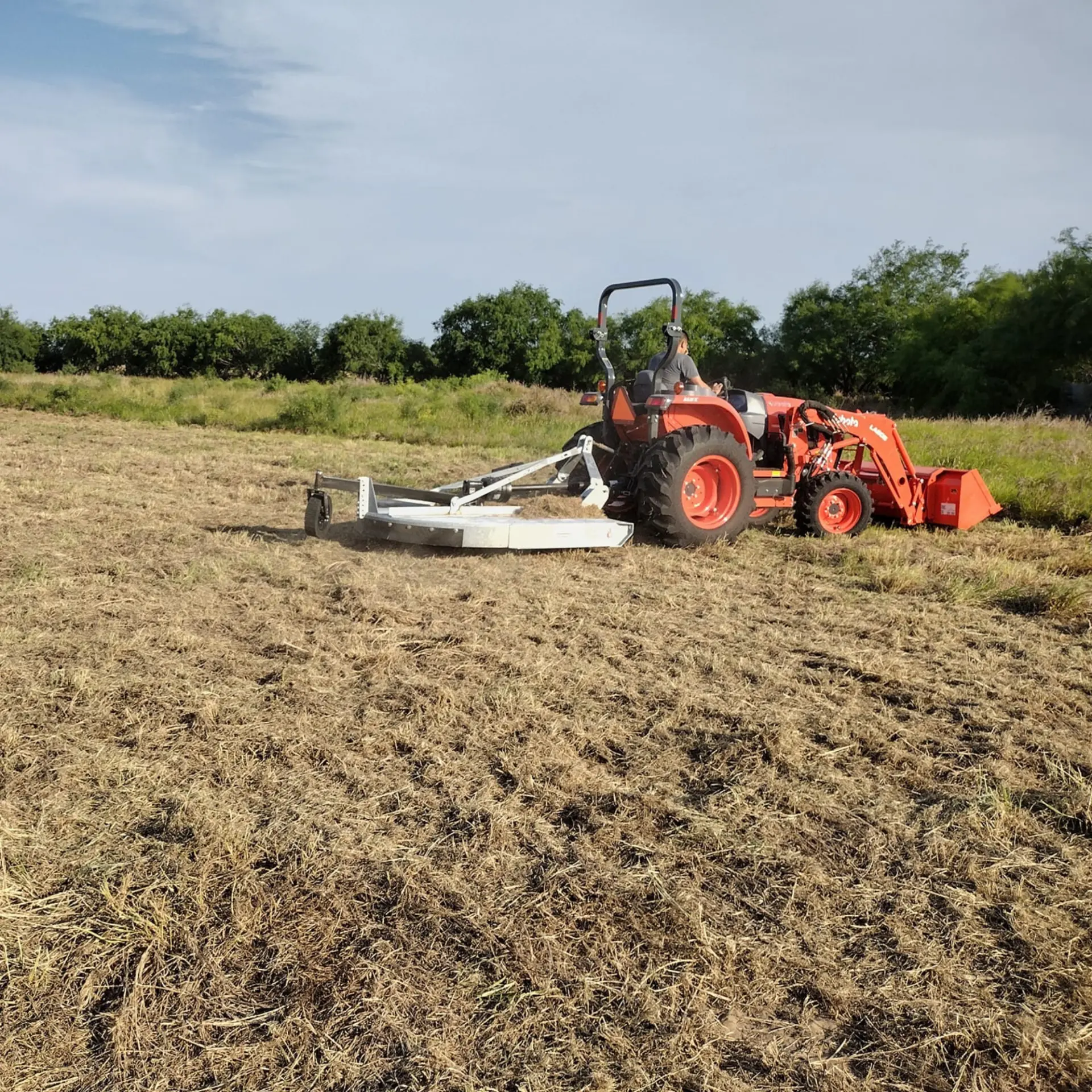 Tractor with a rotary cutter shredding an overgrown acreage field