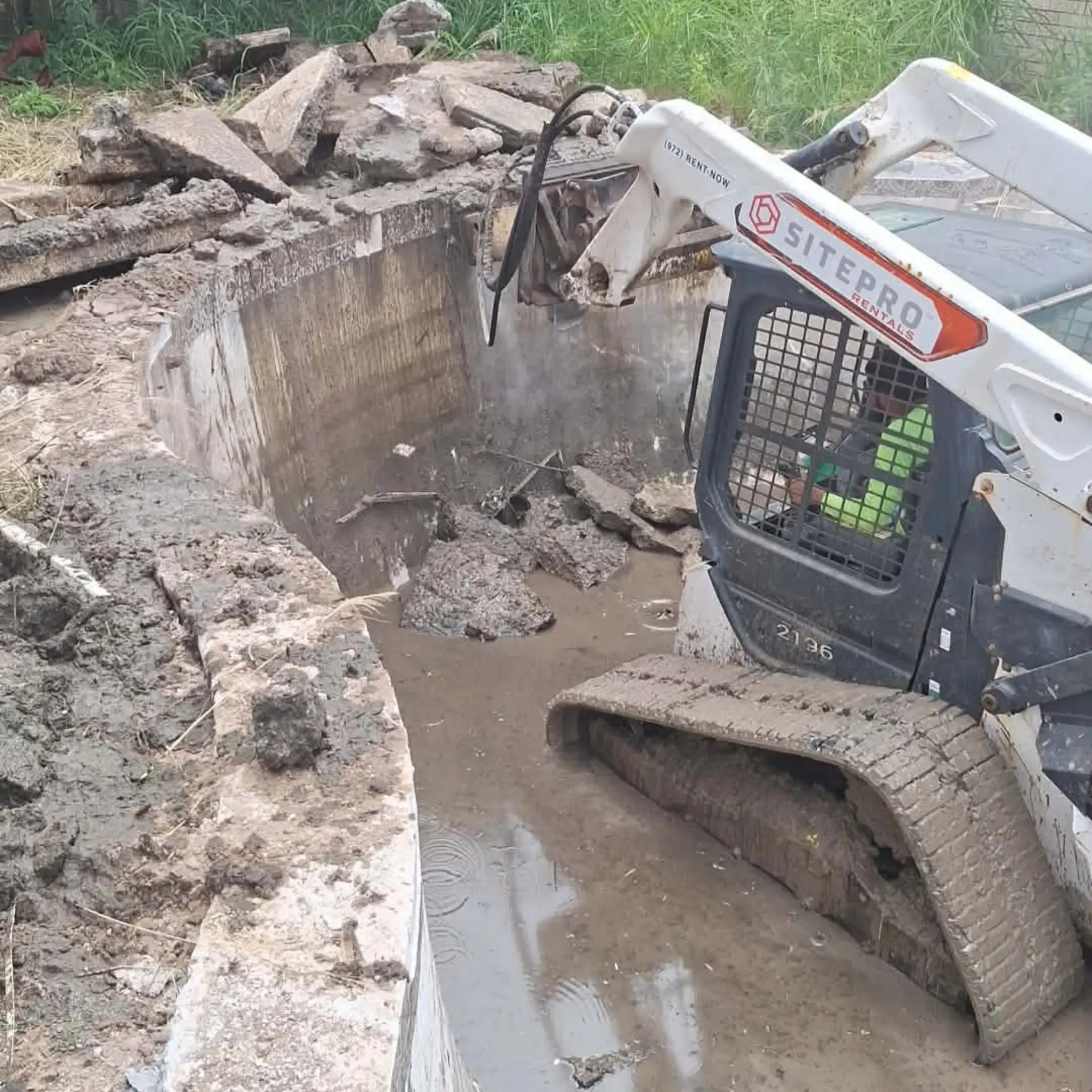 Skid steer with a hydraulic breaker removing a concrete pool shell