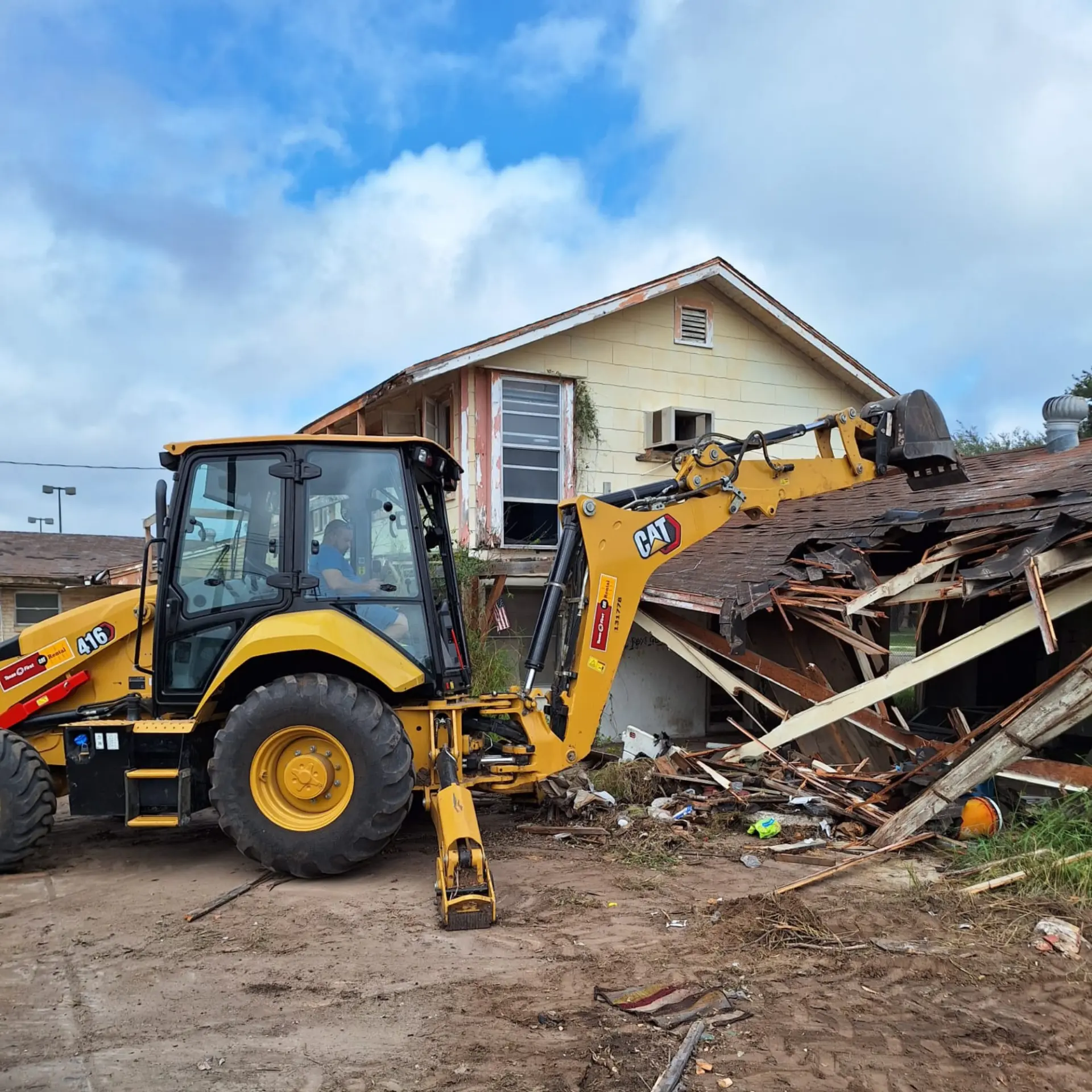 Backhoe dismantling the roof structure of a damaged house