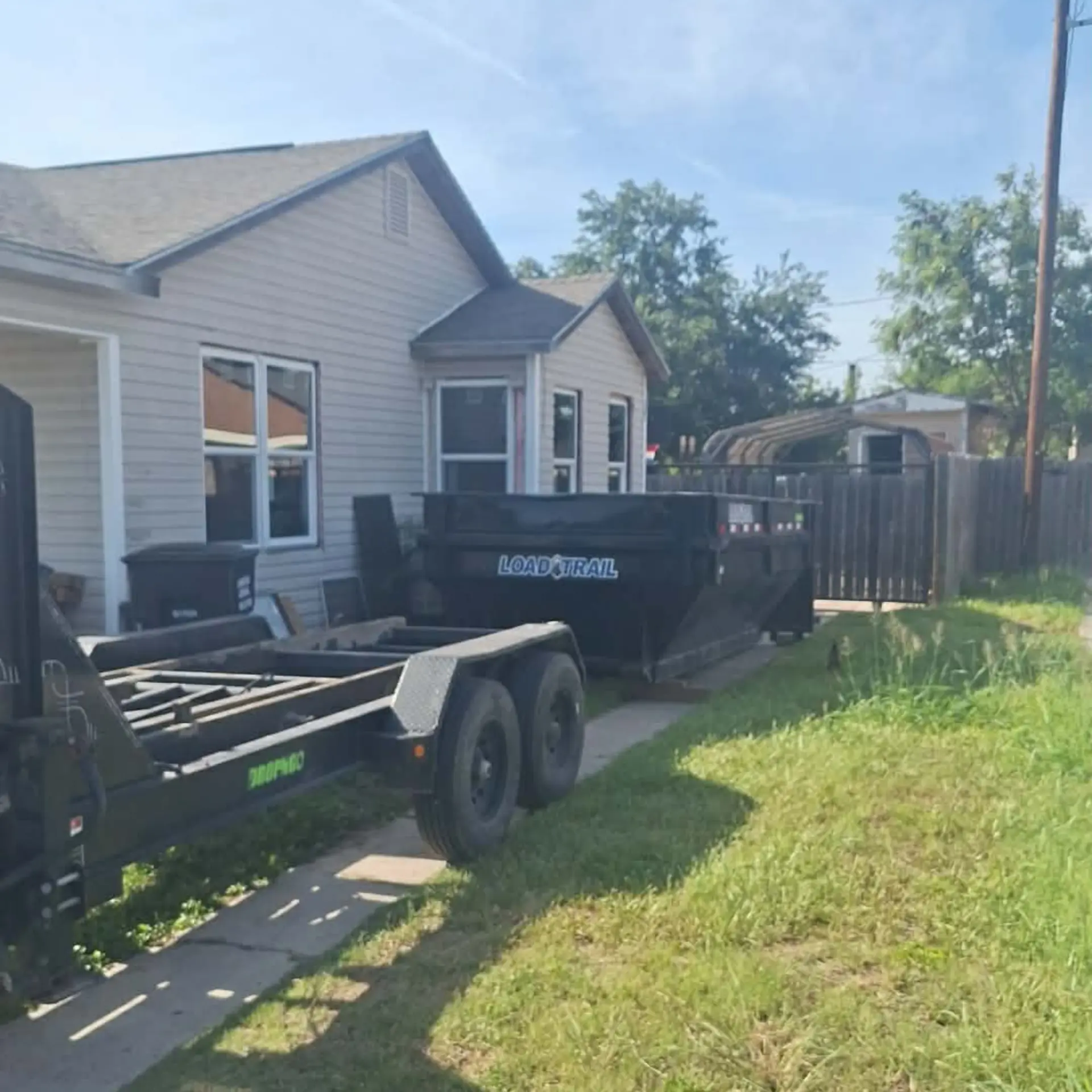 Dump trailer and equipment trailer staged in a driveway for a cleanup rental
